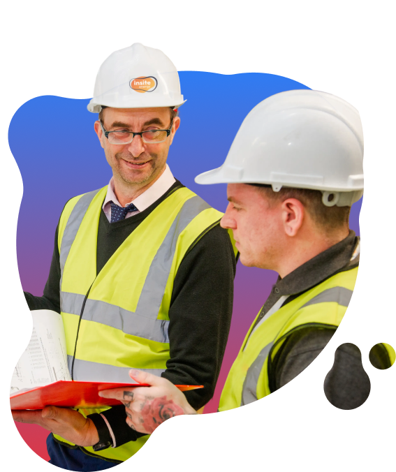 Two engineers wearing hard hats and high‑visibility vests reviewing documents together indoors, with one holding a folder and papers.