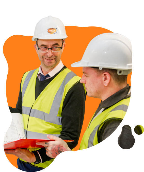 Two engineers wearing hard hats and high‑visibility vests reviewing documents together indoors, with one holding a folder and papers.