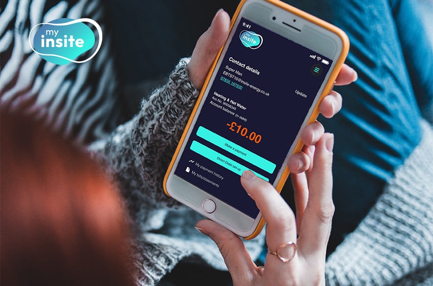 Smartphone held in one hand displaying the 'my insite' energy web-app payment screen, showing account details, a balance of minus £10.00, and buttons labelled “Make a payment” and “View payment history.”