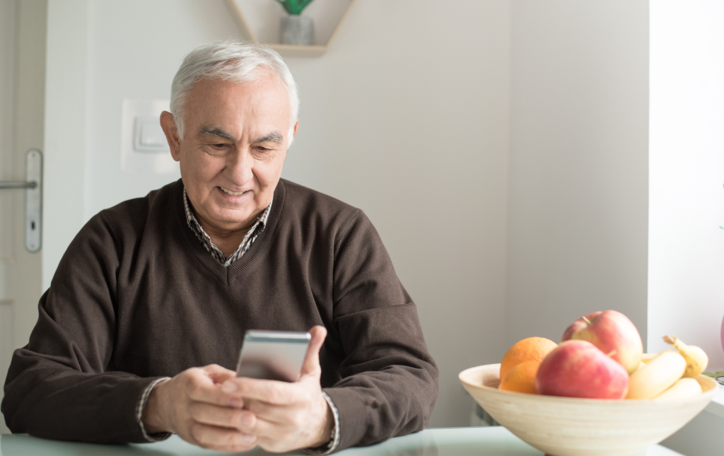 An older gentleman sits on the kitchen counter looking at his phone