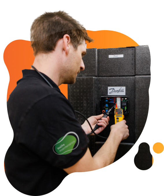 Person adjusting an insulated Danfoss heat interface unit unit using a handheld testing device with cables connected.