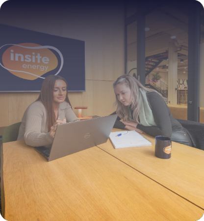 Two people seated at a table using a laptop and reviewing notes during a meeting, with the Insite Energy logo displayed on a screen in the background.