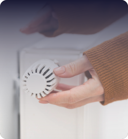Close-up of a hand adjusting a white thermal radiator valve.