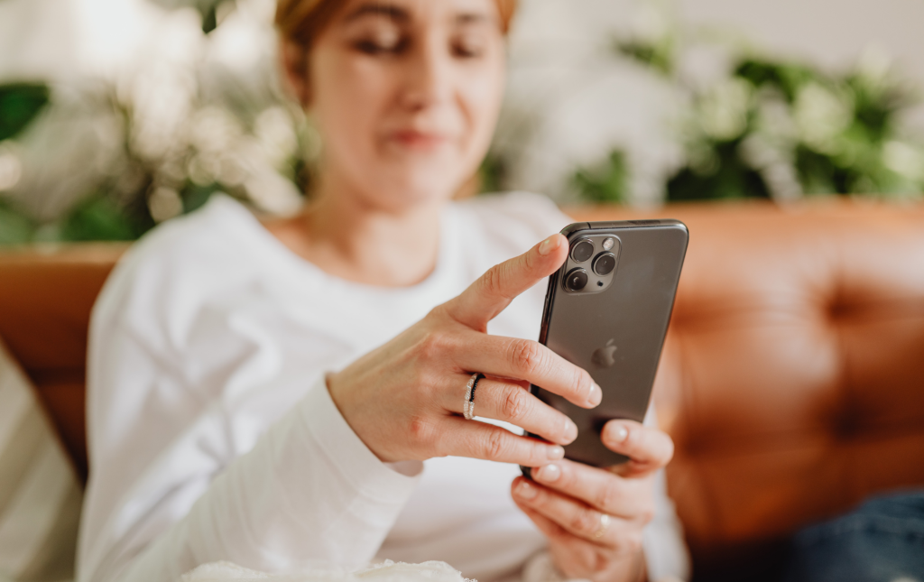 Close-up of a person holding a smartphone with both hands while seated on a sofa, with houseplants visible in the background.