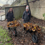 Two Insite employees walking with wheelbarrows filled with dead leaves at Sacrewell Farm.