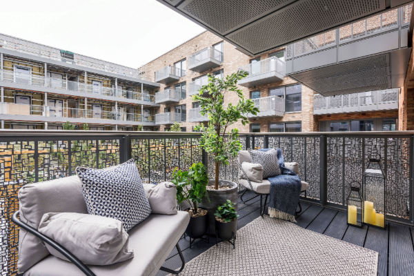 Exterior balcony space at the Stone Studios residential development, showing outdoor seating with cushions, potted plants, and lanterns on a decked terrace, with apartment buildings and balconies visible in the surrounding courtyard.