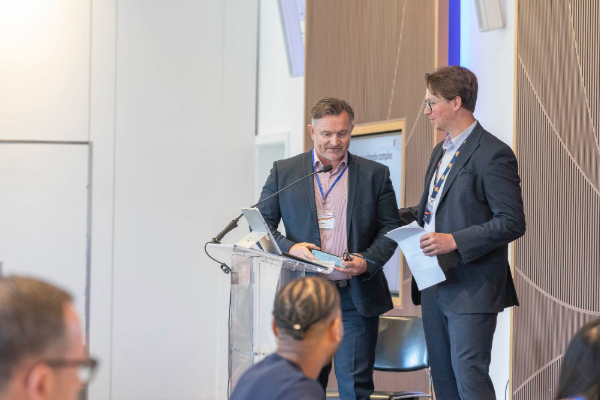 Two presenters (Left: Anthony Atkinson of Telford Homes & Right: Jarrad Bedford of Insite Energy) speaking to an audience during a conference case study session, discussing heat network management and operational challenges at a residential development.